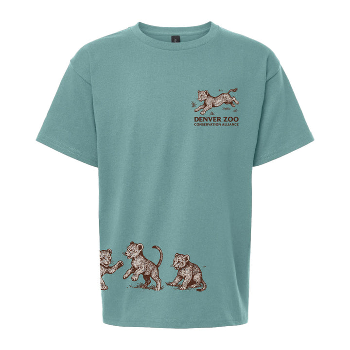 The DZCA Lion Cub Youth T-Shirt is a light blue wildlife tee for kids, featuring three playful lion cubs near the hem, one running cub on the chest, and an official Denver Zoo Conservation Alliance logo above. Ideal for young animal lovers.
