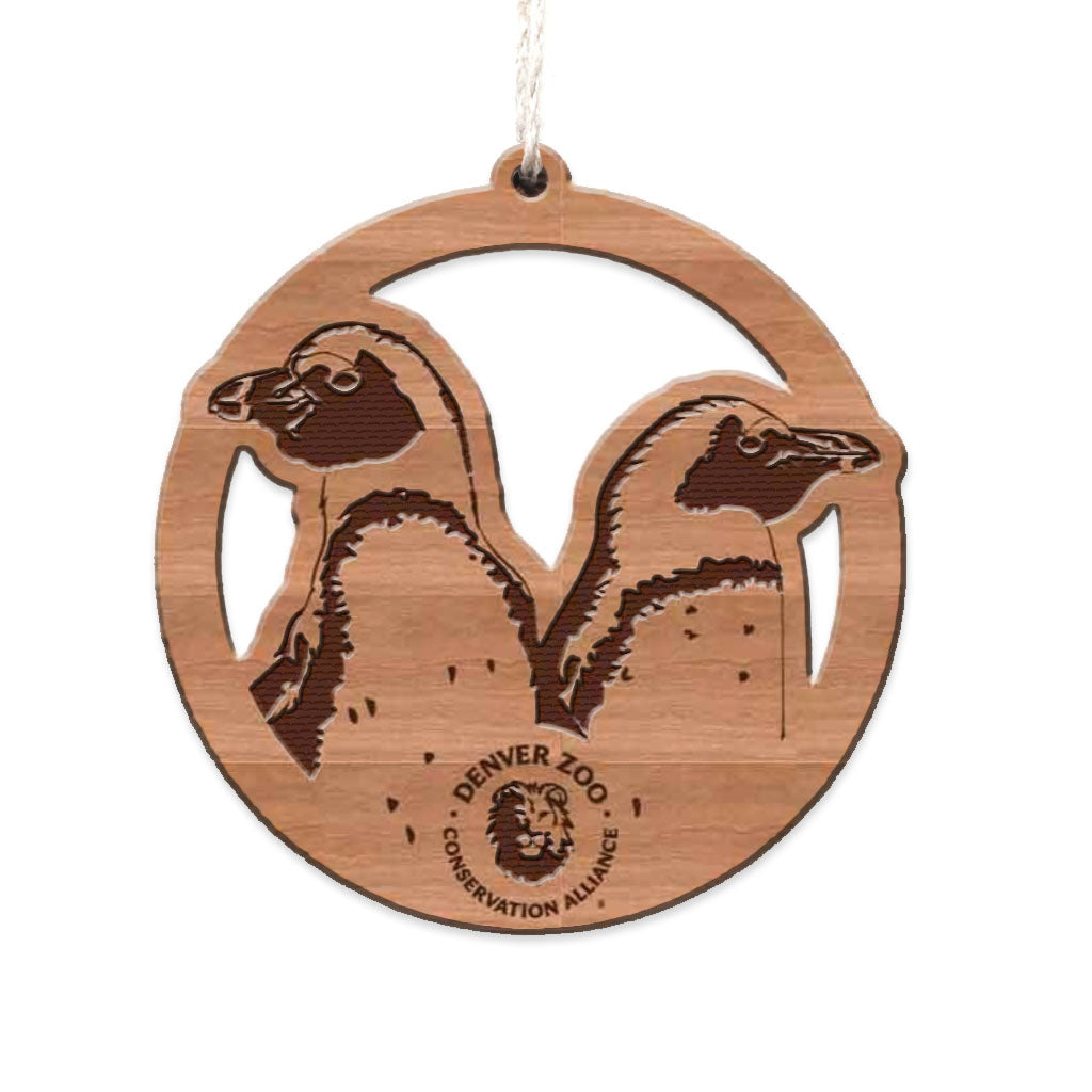 The Wood Penguin Ornament is a handmade wood decoration with two penguins facing opposite ways, "Denver Zoo Conservation Alliance" and a lion logo engraved at the bottom, plus a hanging string—a sustainable holiday ornament.