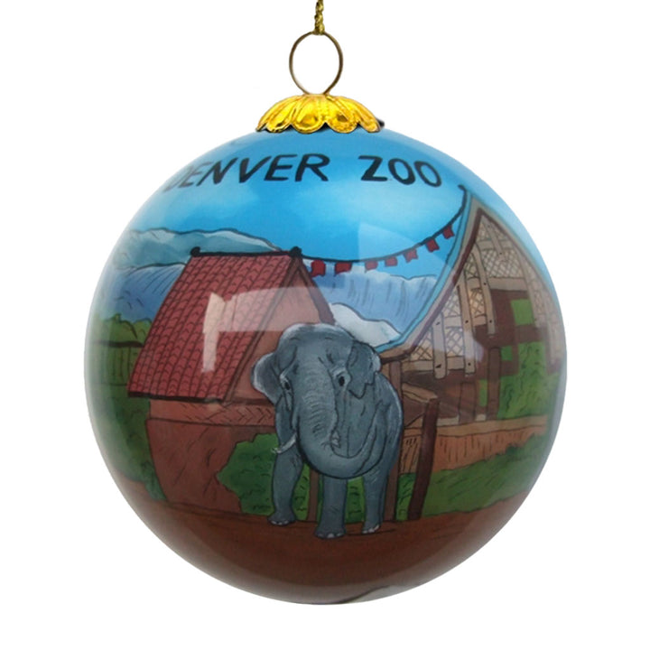 The Denver Zoo Elephant Ornament is a hand-painted glass ornament featuring an elephant in front of a building with "DENVER ZOO" at the top, set against a blue sky and mountain backdrop.