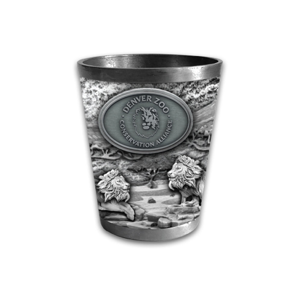 The DZCA Lion Metal Shot Glass features an embossed design with two lions, trees, and "Denver Zoo Conservation Alliance" on an oval plaque on the front.