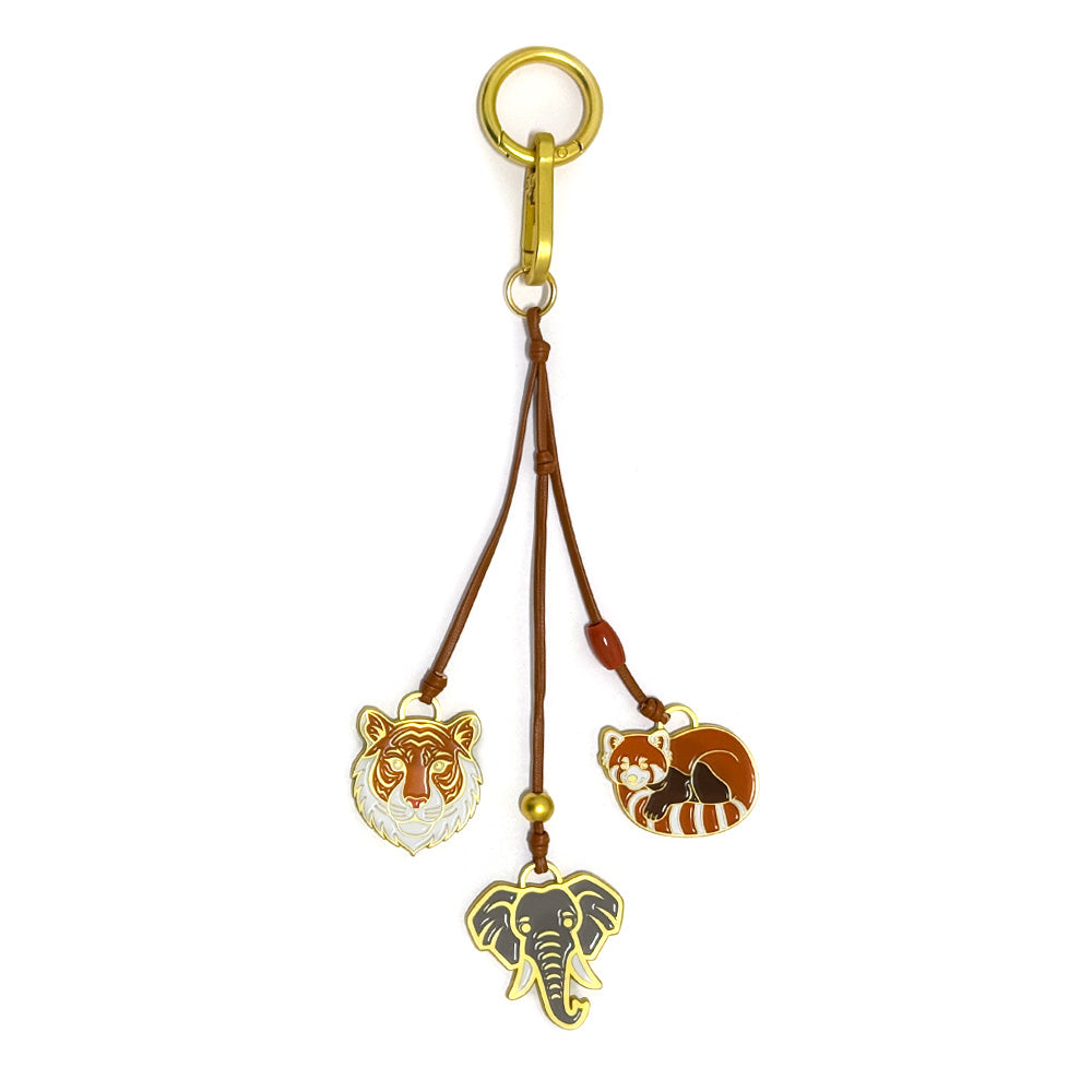 The Zoo Icon Trio Bag Clip features three animal charms—a tiger, red panda, and elephant—dangling from brown cords on a gold keyring and clasp, making a playful accessory for your bag or keys.
