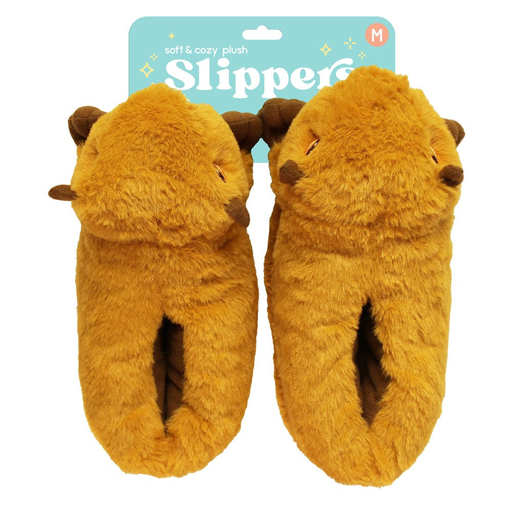 A pair of Capybara Slippers in brown, shaped like capybara faces with cute ears and embroidered eyes, shown with packaging labeled "Soft & cozy Capybara Plush Slipper" in the background.