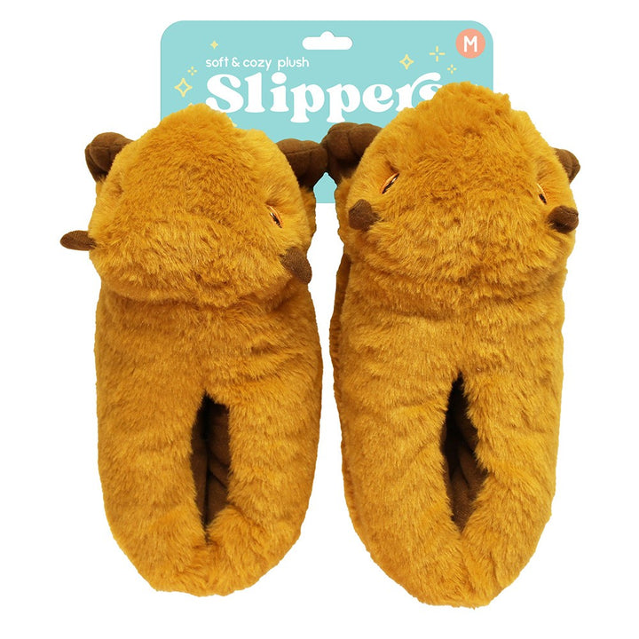 A pair of Capybara Slippers in brown, shaped like capybara faces with cute ears and embroidered eyes, shown with packaging labeled "Soft & cozy Capybara Plush Slipper" in the background.