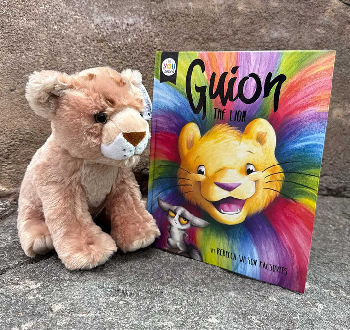 The Guion the Lion Adoption Bundle includes a plush African lion cub and the colorful children's book "Guion the Lion" by Rebecca Wilson Macsovits, featuring an illustrated lion with a rainbow mane and a small character on the cover.