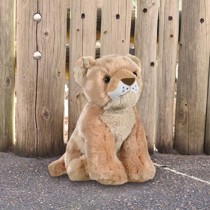 A plush lion with a gentle expression sits by a wooden fence, legs stretched out—perfect for the Birthday Adoption Bundle or inspiring kids to Adopt an Animal.