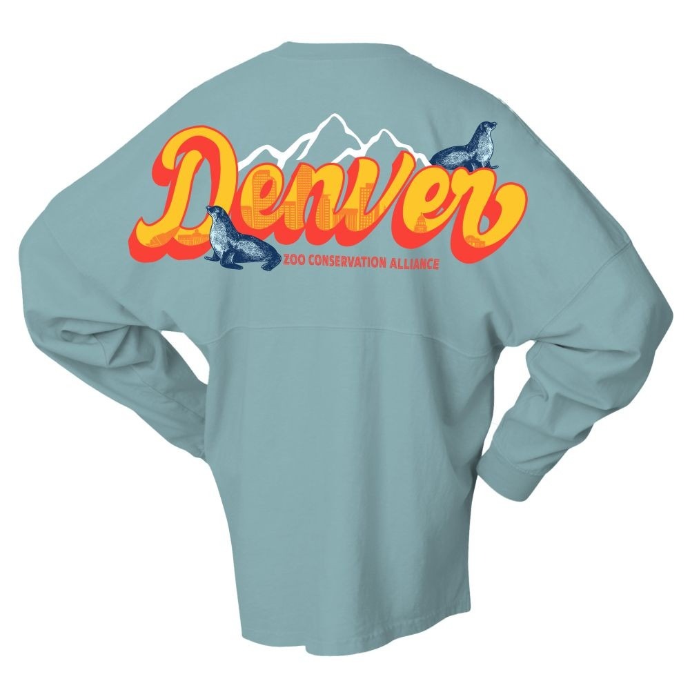 The DZCA Sea Lion Spirit Jersey is a light blue top with “Denver” in bold orange/yellow, mountains, two seals, and “Zoo Conservation Alliance” on the back—honoring marine mammal conservation at Denver Zoo.