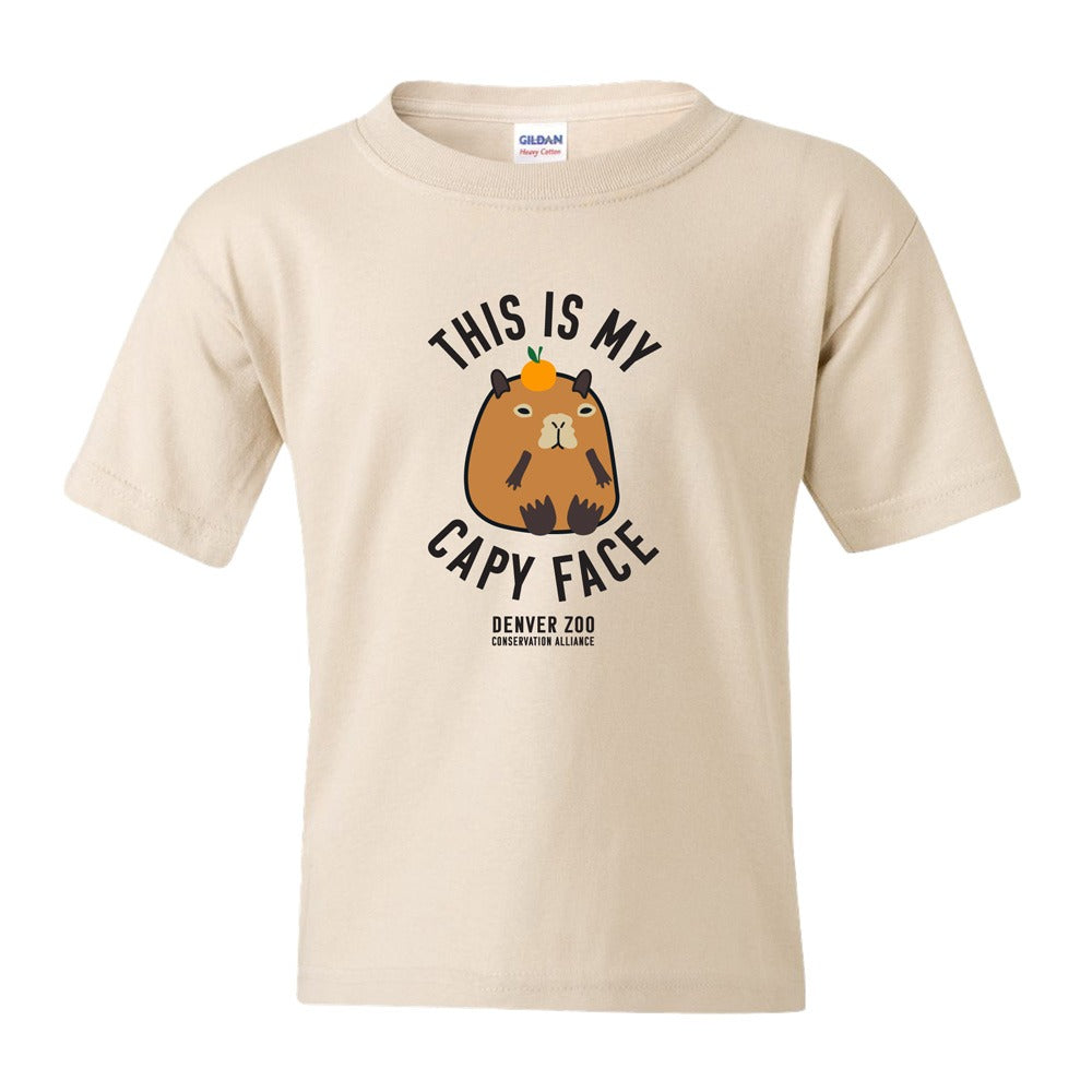 The DZCA Capybara Face Youth T-Shirt is a beige unisex cotton tee featuring a cartoon capybara with a yellow bird and “THIS IS MY CAPY FACE” above, “DENVER ZOO CONSERVATION ALLIANCE” below—ideal for animal lovers.