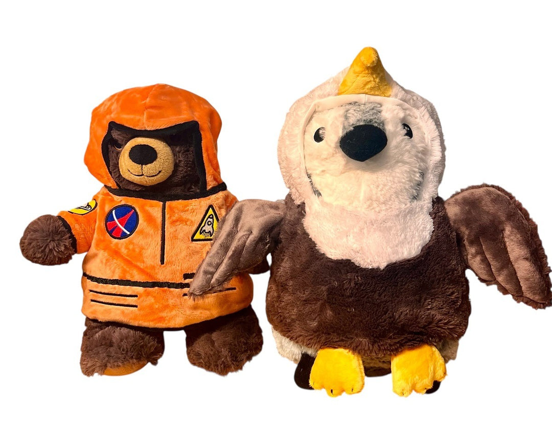 Two plush toys—a brown bear in an orange astronaut suit with patches, and a brown and white bird with yellow feet and beak—are ready to dress up in the Plush Giraffe Outfit for extra playful fun.