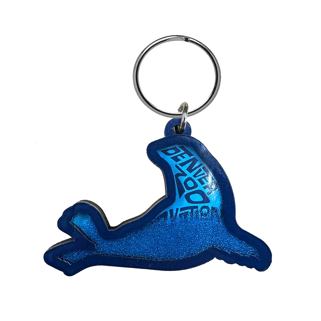 A blue DZCA Sea Lion Keychain, shaped like a seal with a silver keyring and "GENOA" in uppercase on its body—perfect for showing your support for wildlife conservation.