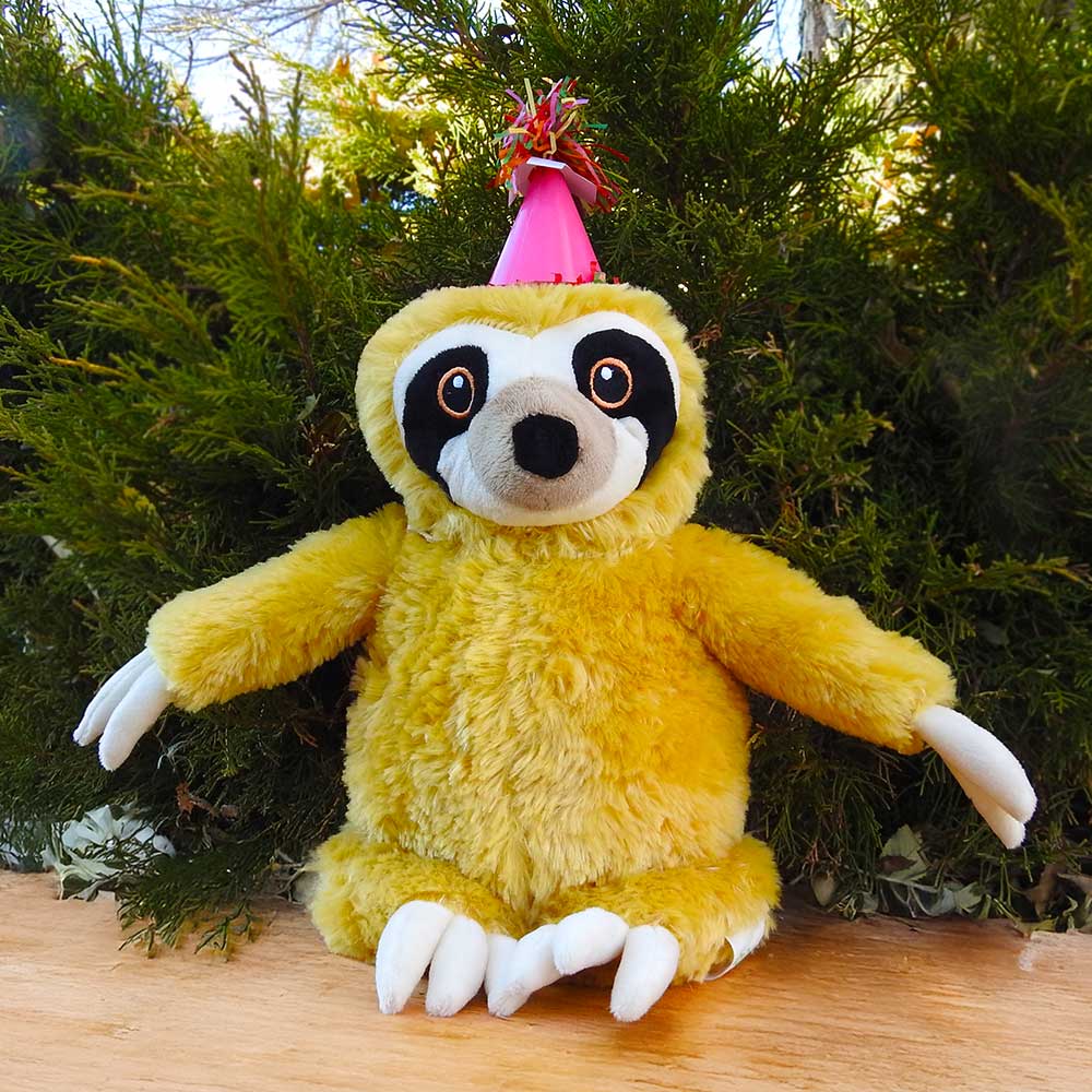 A yellow plush sloth in a pink party hat sits on a wooden surface with green bushes behind—an ideal Birthday Adoption Bundle gift for anyone wanting to adopt an animal.